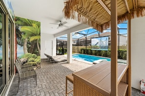 A covered outdoor area with a pool, seating, and a view of a roller coaster. - 7BR Disney Escape  Pool, Spa, Theater & Arcade (Kissimmee)