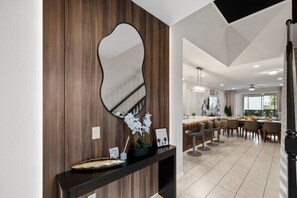 A modern interior with a wooden accent wall, a large mirror, a dining area with chairs, and a kitchen with bar stools. - 7BR Disney Escape  Pool, Spa, Theater & Arcade (Kissimmee)