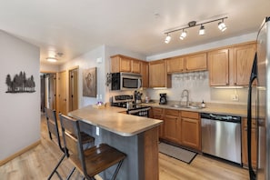 A modern kitchen with wooden cabinets, stainless steel appliances, a central island with bar stools, and pendant lighting. - Ground Level | On Bus Route | 3 SmartTVs | Updated (Steamboat Springs)