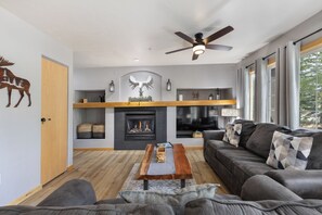 A modern living room with a fireplace, a ceiling fan, and a large window. - Ground Level | On Bus Route | 3 SmartTVs | Updated (Steamboat Springs)