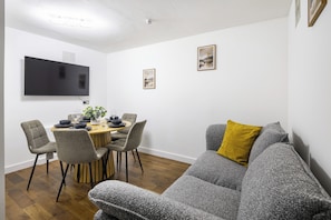 A modern living room with a grey sofa, a dining table set for four, and a flat-screen TV mounted on the wall. - Central London 2-Bedroom Apartment on Leather Lane | Sleeps 6 | (London)