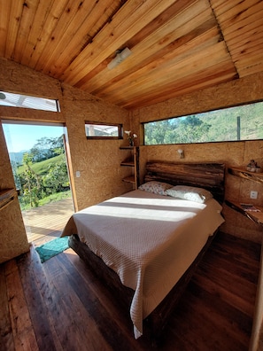 A wooden cabin bedroom with a bed, a window, and a view of greenery.