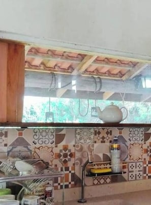 A kitchen with a tiled backsplash, a hanging pot rack, and various kitchen items on the counter.