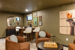 A cozy living room with a bar area, comfortable seating, and a chess table. - Denver Dream Retreat w/Hot Tub, Sauna, Movie & Game Rms, Putting Green, Fire Pit (Arvada)