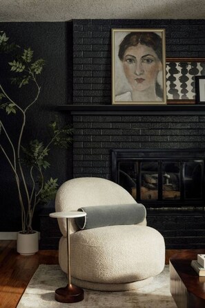 A modern living room with a dark brick fireplace, a white armchair, and a potted plant. - Denver Dream Retreat w/Hot Tub, Sauna, Movie & Game Rms, Putting Green, Fire Pit (Arvada)