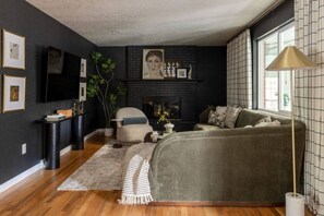 A modern living room with a dark wall, a fireplace, a sofa, a coffee table, and a television. - Denver Dream Retreat w/Hot Tub, Sauna, Movie & Game Rms, Putting Green, Fire Pit (Arvada)