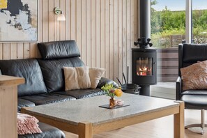 A cozy living room with a leather sofa, a coffee table with a vase, and a wood-burning stove. - Lovely holiday home with hot tub in Skaven Strand (Tarm)