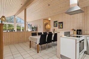 A modern kitchen with a dining area, wooden paneling, and large windows. - Lovely holiday home with hot tub in Skaven Strand (Tarm)