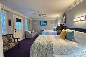 Een hotelkamer met een bed, een bank, een televisie en een plafondventilator.