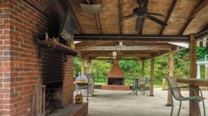 Eine Terrasse im Freien mit Kamin aus Ziegelsteinen, Deckenventilator und Grillplatz.