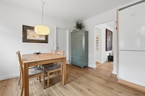 A dining area with a wooden table and chairs, a hanging light fixture, and a cabinet with a plant. - Cozy and spacious house (Vrå)