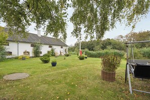 A white building with a sloped roof, surrounded by a well-maintained lawn and various potted plants. - Cozy and spacious house (Vrå)