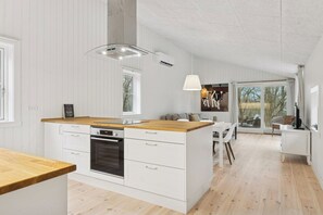A modern kitchen with white cabinetry, a wooden countertop, and a built-in oven. - Architect-designed luxury summerhouse in Ordrup (Fårevejle)
