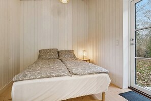A bedroom with a bed, a nightstand, and a window with a view of trees. - Architect-designed luxury summerhouse in Ordrup (Fårevejle)