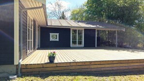 A wooden deck with a covered area, a window, and a door. - Architect-designed luxury summerhouse in Ordrup (Fårevejle)