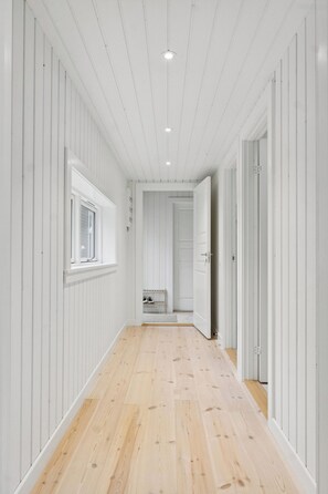 A hallway with wooden flooring and white walls, leading to a room with a window and a door. - Architect-designed luxury summerhouse in Ordrup (Fårevejle)