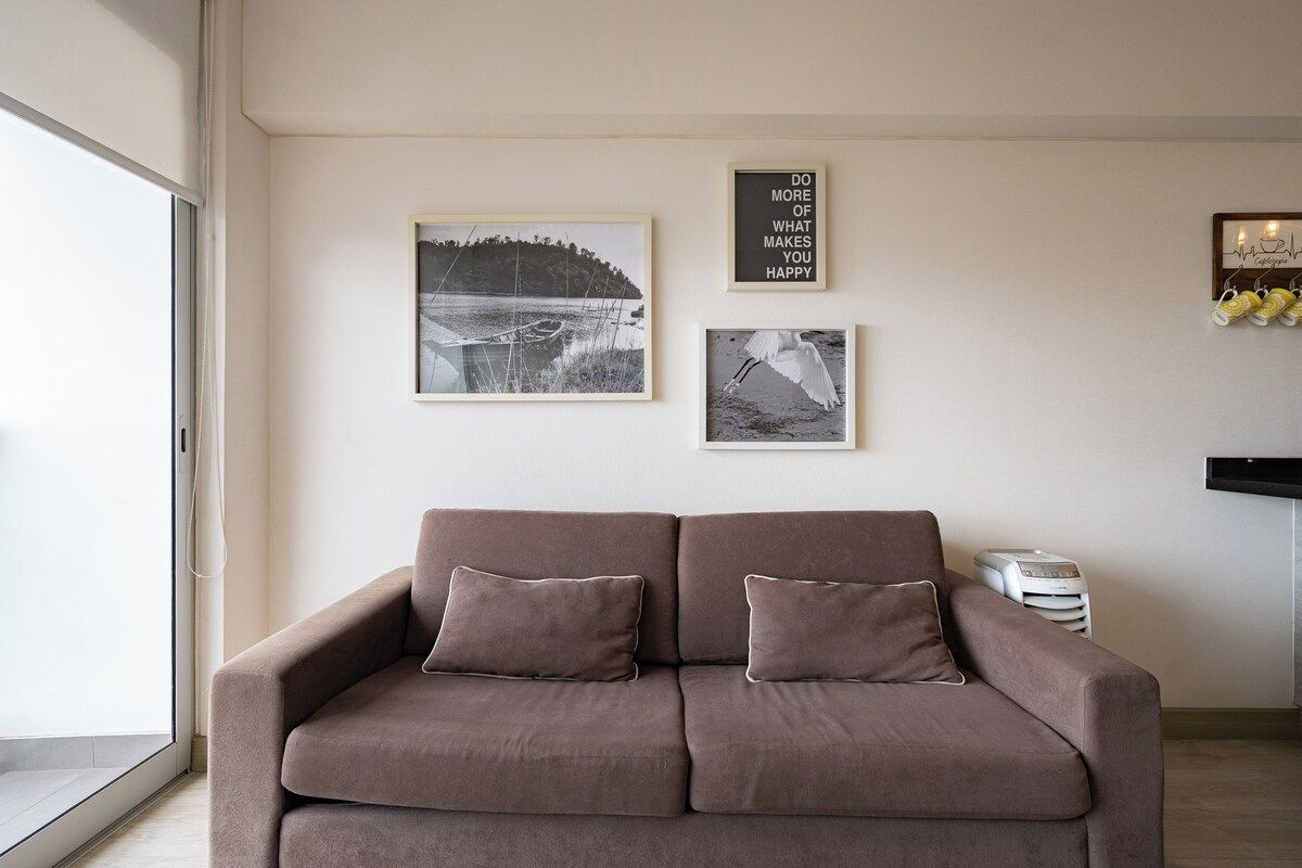 Un salon avec un canapé marron, deux coussins et trois tableaux encadrés accrochés au mur.