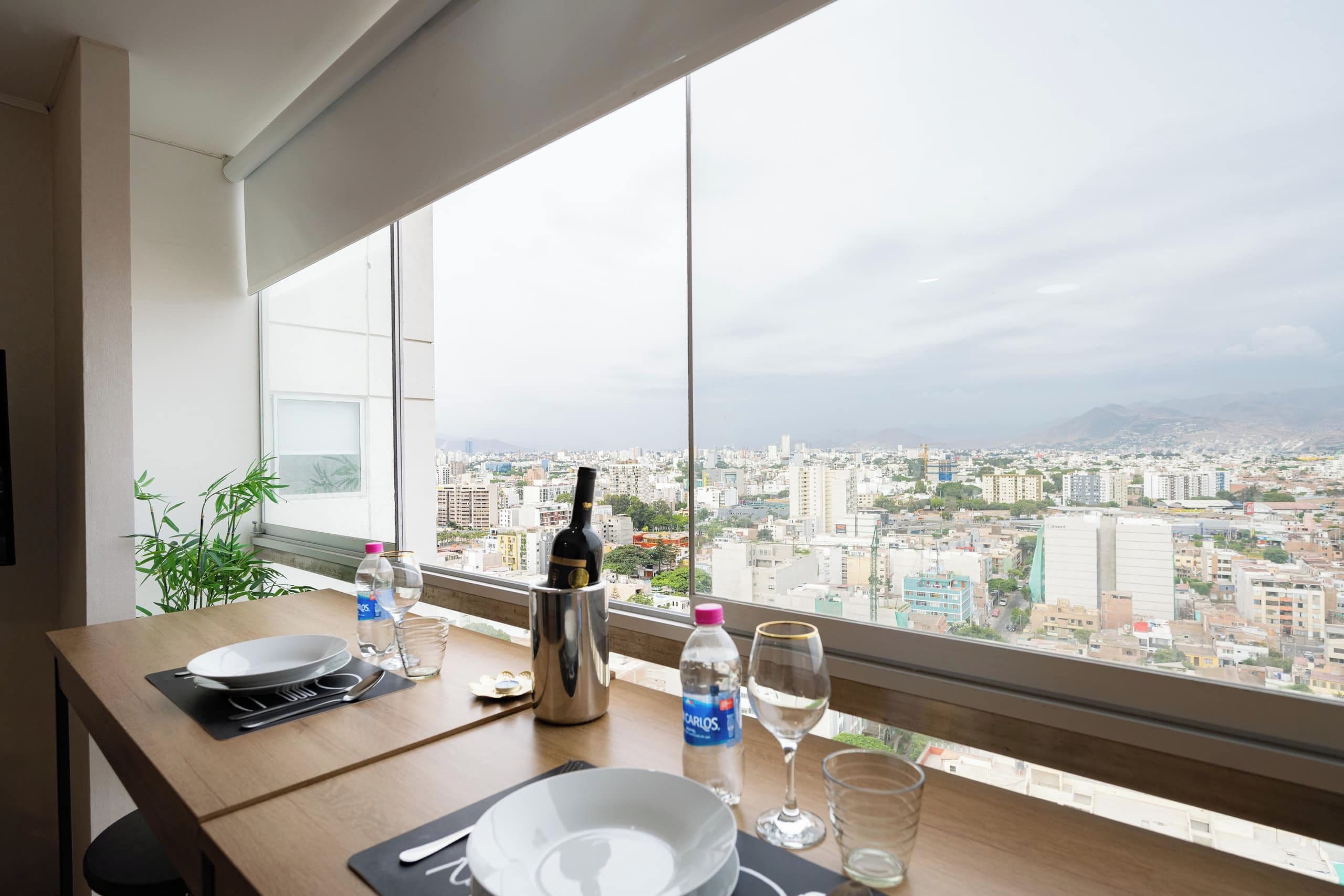 Une table à manger avec vue sur la ville, une bouteille d’eau, un verre à vin et une bouteille d’alcool.