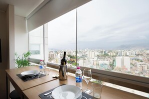 A dining table with a city view, a bottle of water, a wine glass, and a bottle of alcohol. - Connect Apartments by Vibrant (Barranco)