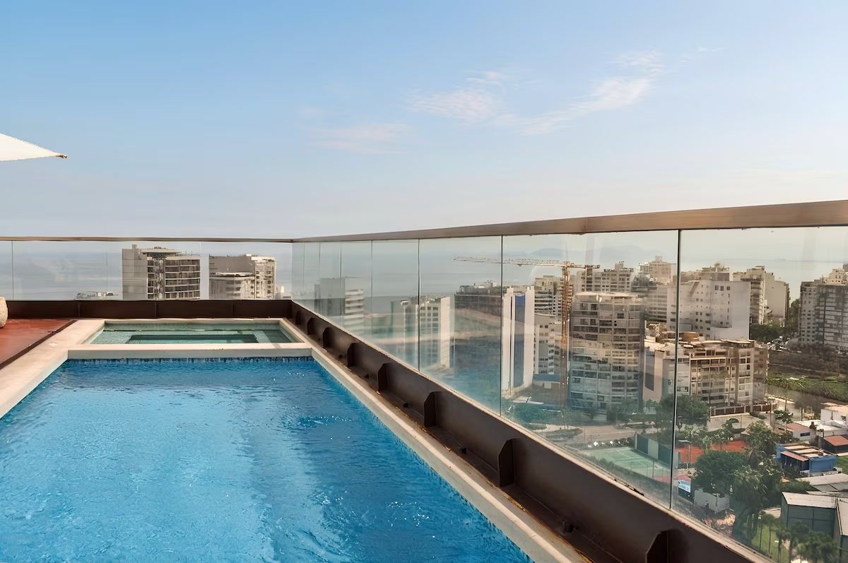 Una piscina en la azotea con barandilla de cristal y vistas panorámicas de la ciudad.