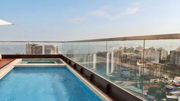 Una piscina en la azotea con barandilla de cristal y vistas panorámicas de la ciudad.