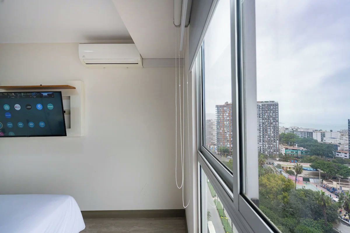 Een hotelkamer met een groot raam, een bed, een wandtelevisie en een airconditioner.