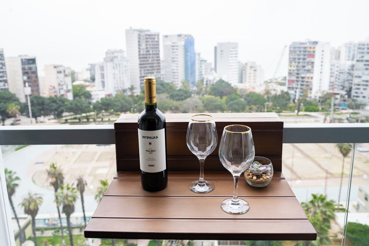 Een fles wijn en twee glazen op een balkon met uitzicht over de stad.