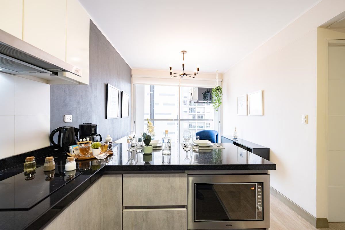 A modern kitchen with a built-in oven, a coffee maker, and a dining area with a blue chair.