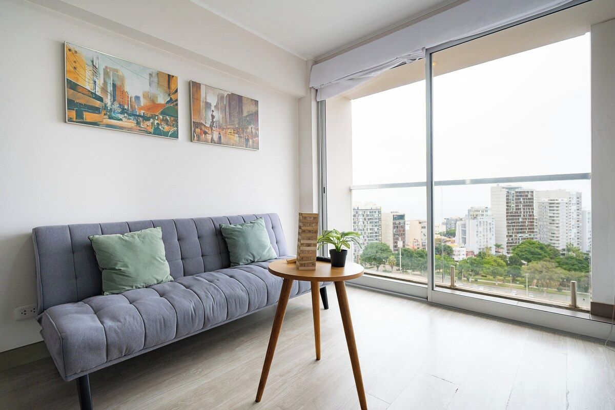 Una sala de estar moderna con un sofá gris, una mesita redonda y dos cuadros en la pared.