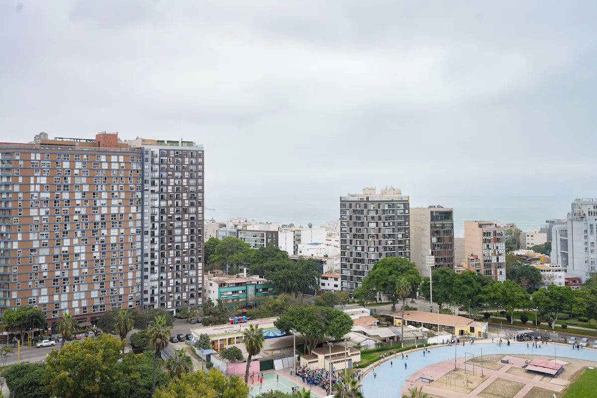 Een hoog appartementencomplex met meerdere balkons, omringd door groen en andere gebouwen.