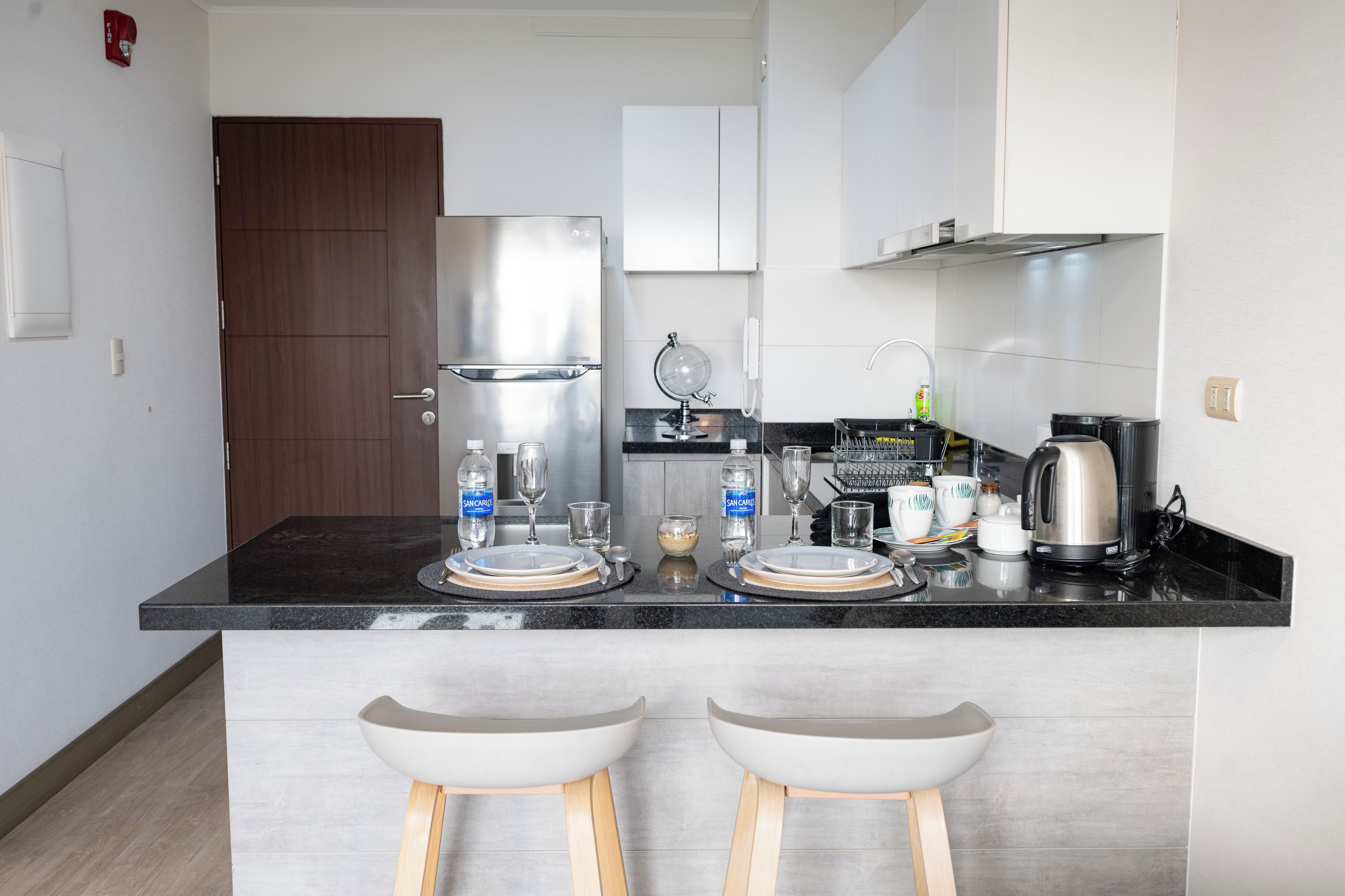 Een moderne keuken met een zwart aanrecht, roestvrijstalen apparatuur en twee witte barkrukken.