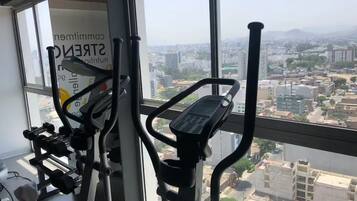 A gym with exercise equipment and a large window offering a city view.