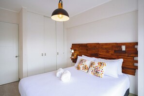 Une chambre d’hôtel avec un lit, une tête de lit en bois, du linge de lit blanc et un luminaire suspendu.