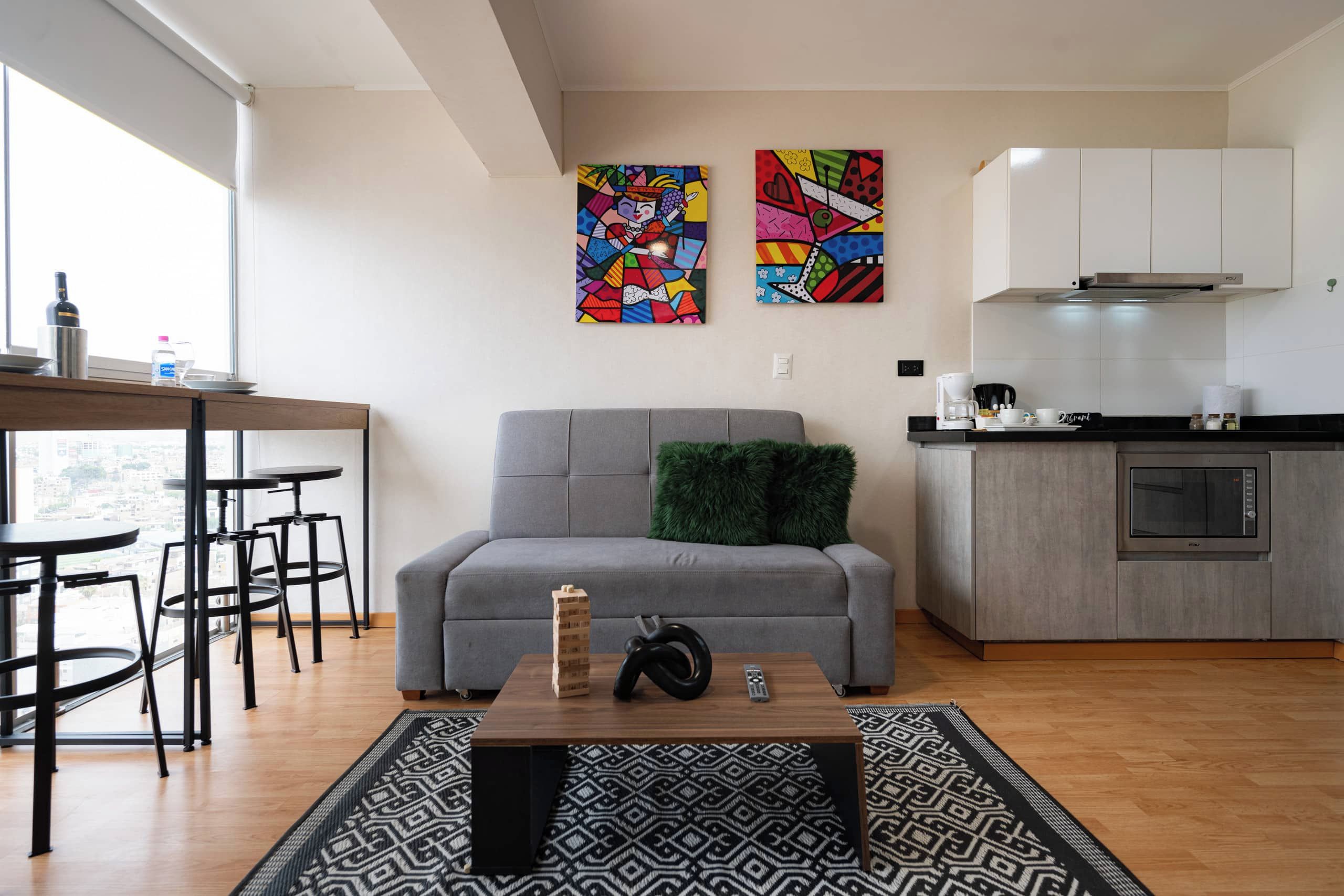 A modern living space with a grey sofa, a coffee table, and a kitchen area with a microwave and cabinets.