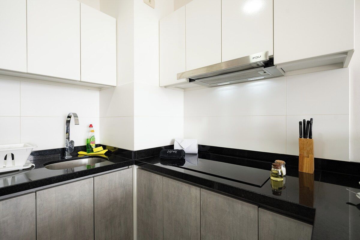 Una cocina moderna con armarios de acero inoxidable, encimera negra y campana extractora empotrada.