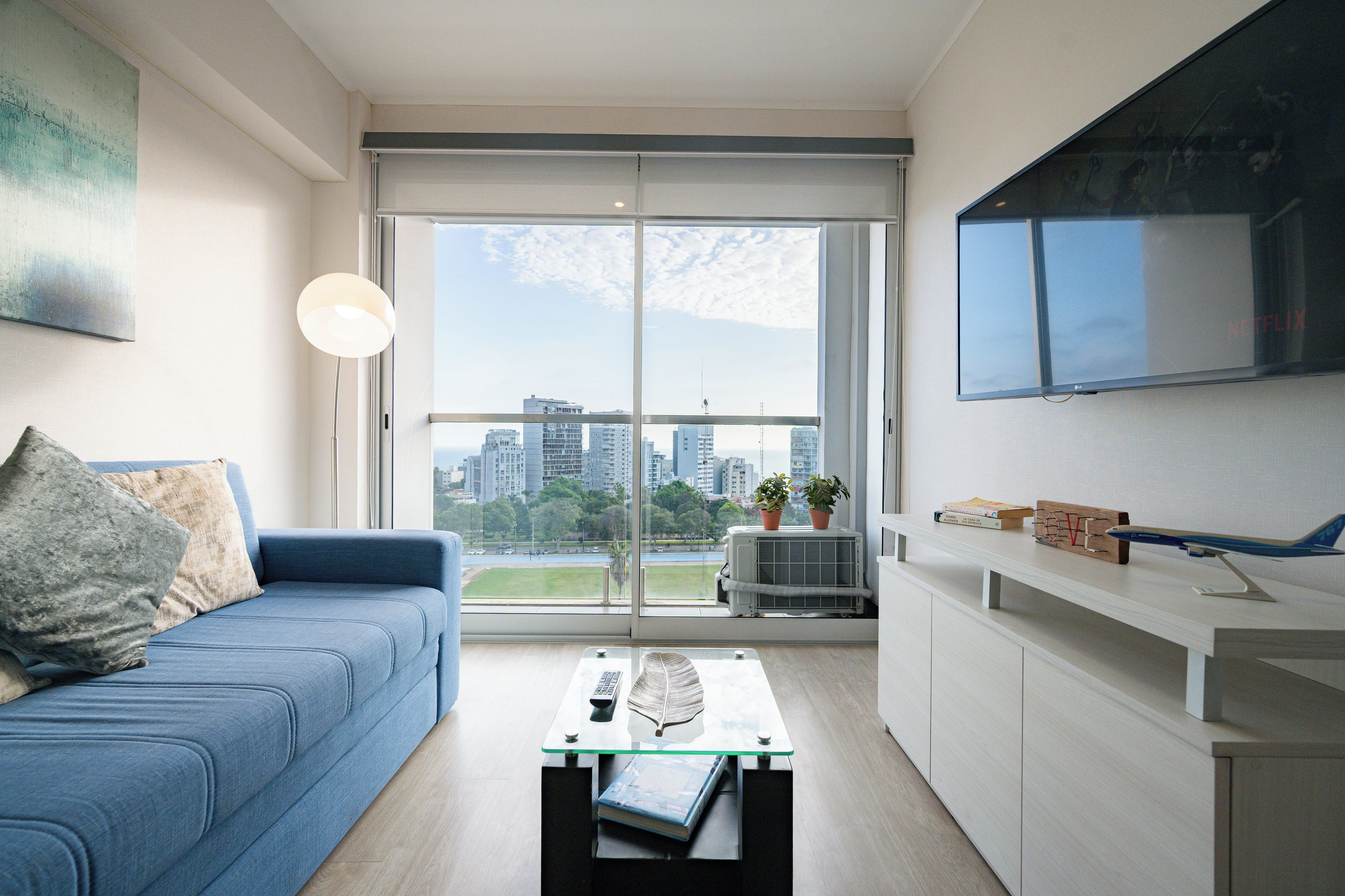 Een moderne woonruimte met een bank, een salontafel, een flatscreen-televisie en een uitzicht op de skyline door grote ramen.