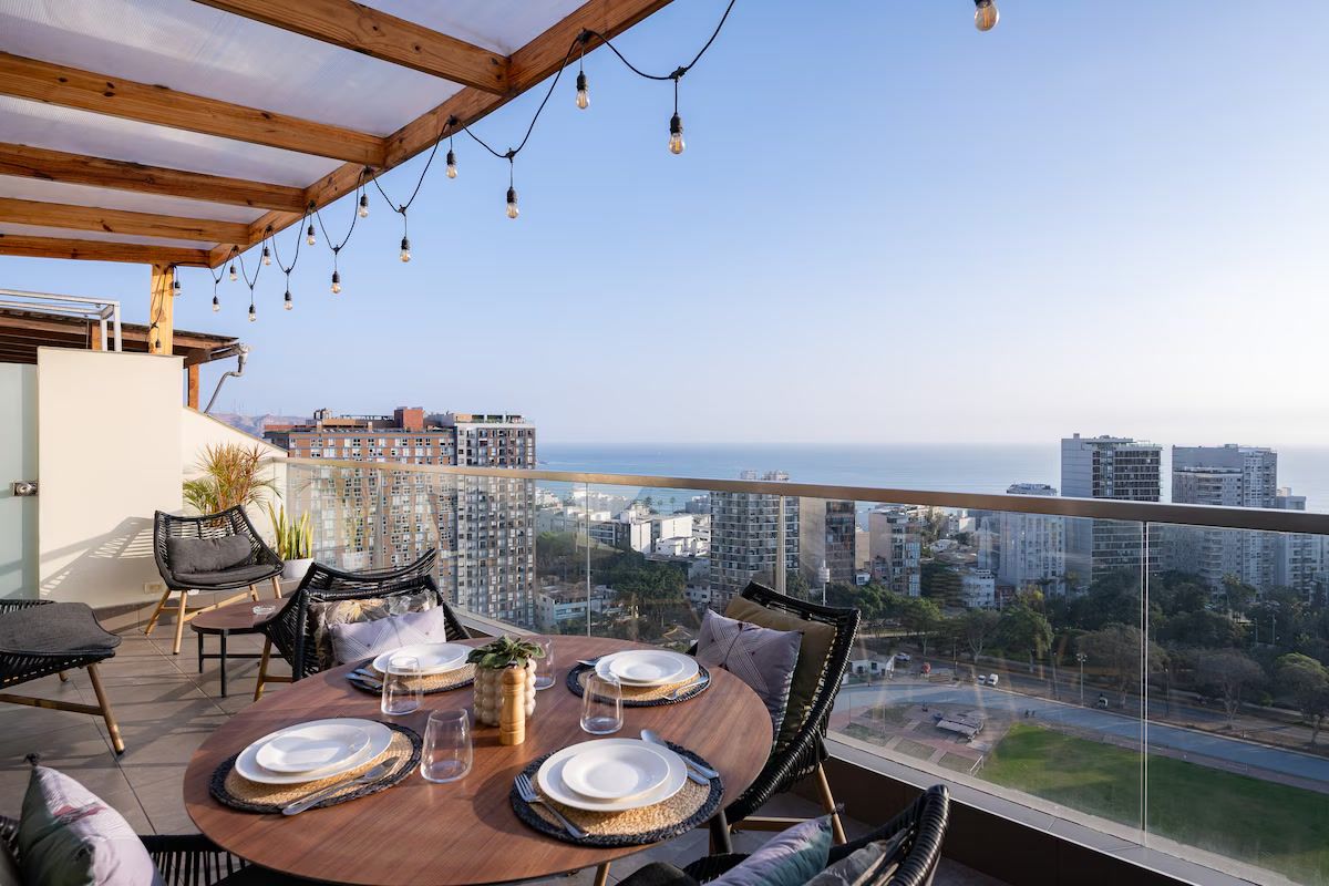 Zona de dinar amb taula preparada per a quatre persones, amb vista a un paisatge urbà i al mar.