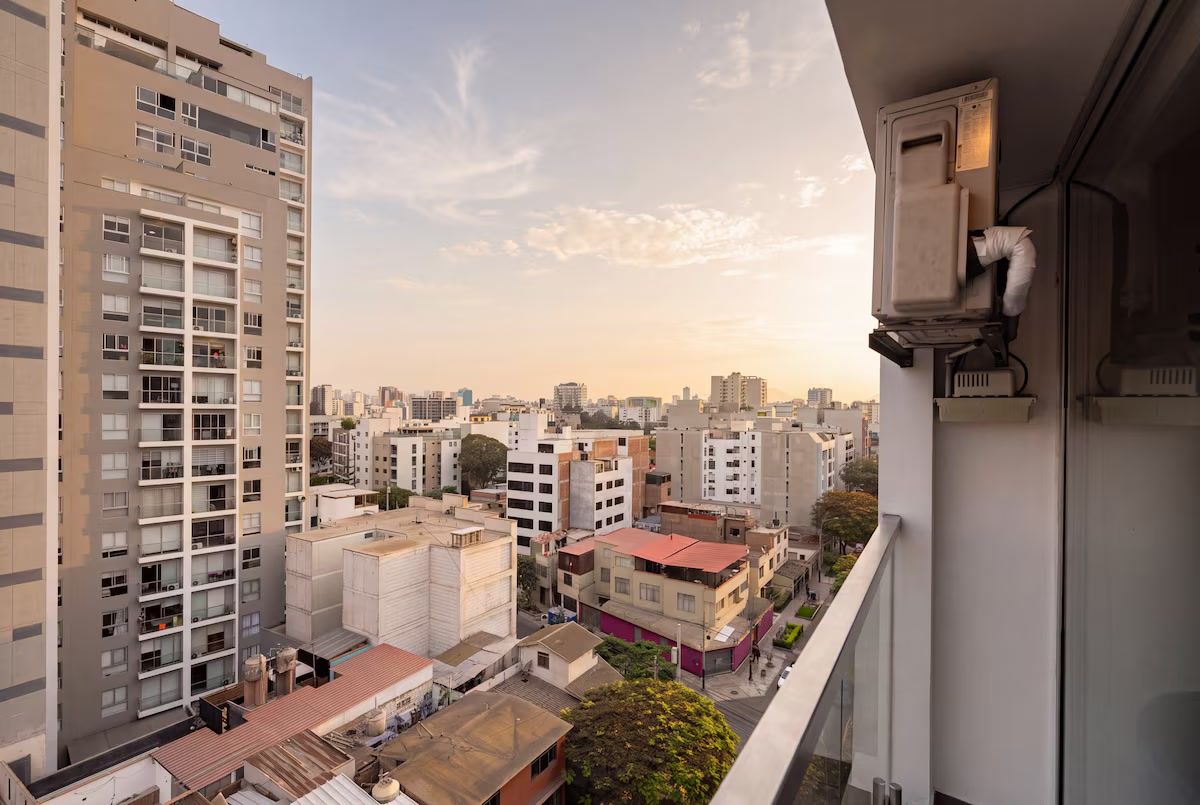 Un edificio de gran altura con varios pisos y balcones, con vista a una zona urbana densamente poblada y diversos edificios.
