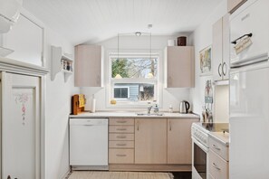 A compact kitchen with a dishwasher, stove, and a window providing natural light. - Lovely holiday oasis on scenic Thyholm (Thyholm)