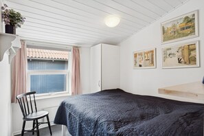 A bedroom with a bed, a chair, a window with curtains, and wall-mounted pictures. - Lovely holiday oasis on scenic Thyholm (Thyholm)