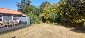 En inglasad uteplats med utemöbler, en inhägnad trädgårdsdel och ett hus med ett rött tak.