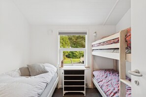 Ein Schlafzimmer mit zwei Etagenbetten, einem Schreibtisch und einem Fenster mit Blick auf Grünflächen.