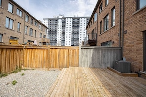 A backyard with a wooden deck, a gravel area, and a tall residential building in the background.