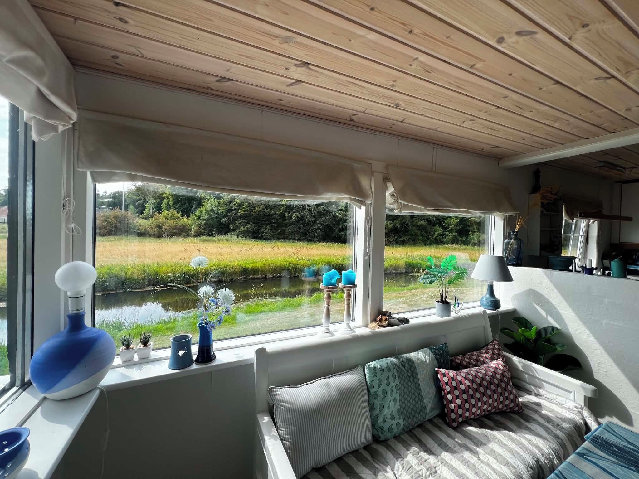 A room with a view of a river, a wooden ceiling, and a seating area with cushions.
