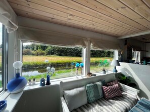A room with a view of a river, a wooden ceiling, and a seating area with cushions. - Cozy cottage by the Trend River (Løgstør)
