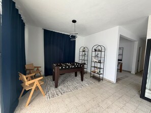 Ein Zimmer mit einer Fußballstoßmaschine, zwei Stühlen, einem dunkelblauen Vorhang, einer weißen Decke und einem gemusterten Teppich.