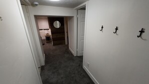 Un pasillo con piso alfombrado, paredes blancas y una puerta que conduce a una habitación con un espejo circular.
