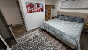 Un dormitorio con cama, mesita de noche, armario, puerta y estante montado en la pared.