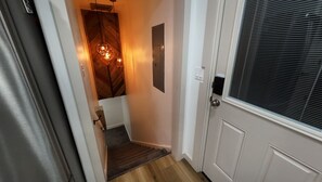 Ein schmaler Gang mit einer Holztreppe, einer Tür mit Fenster und einer Leuchte.