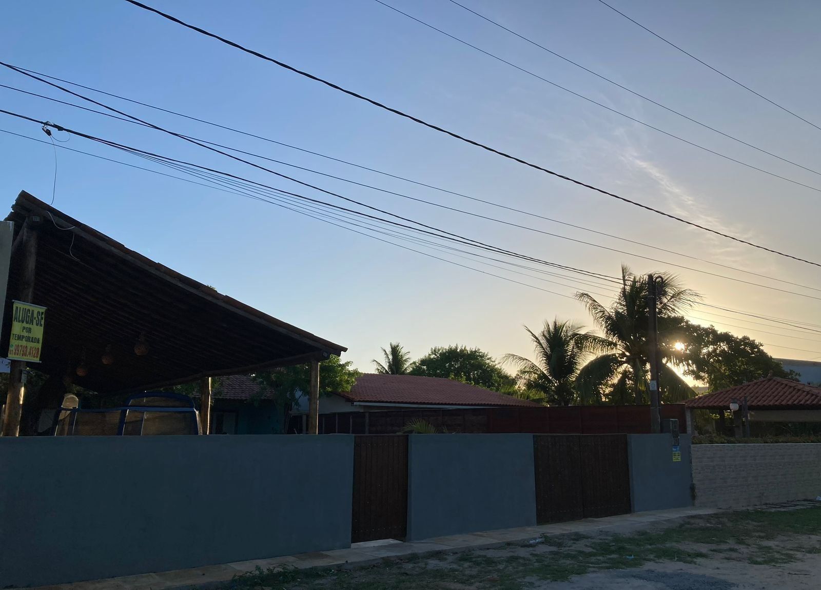 Un edificio con techo de metal y un cartel, rodeado por un muro bajo y una cerca.